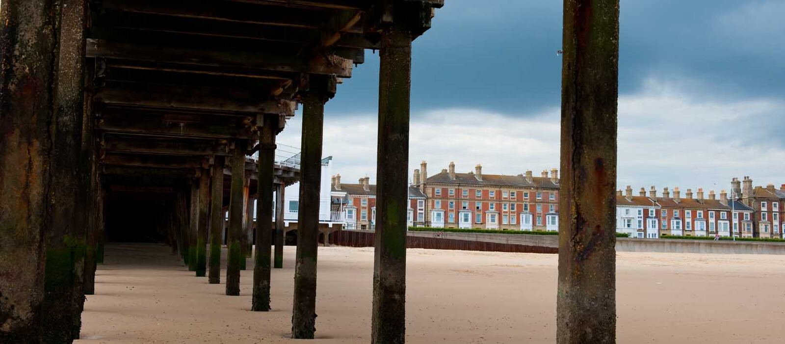 Under a wooden pier looking out to a seafront terrace